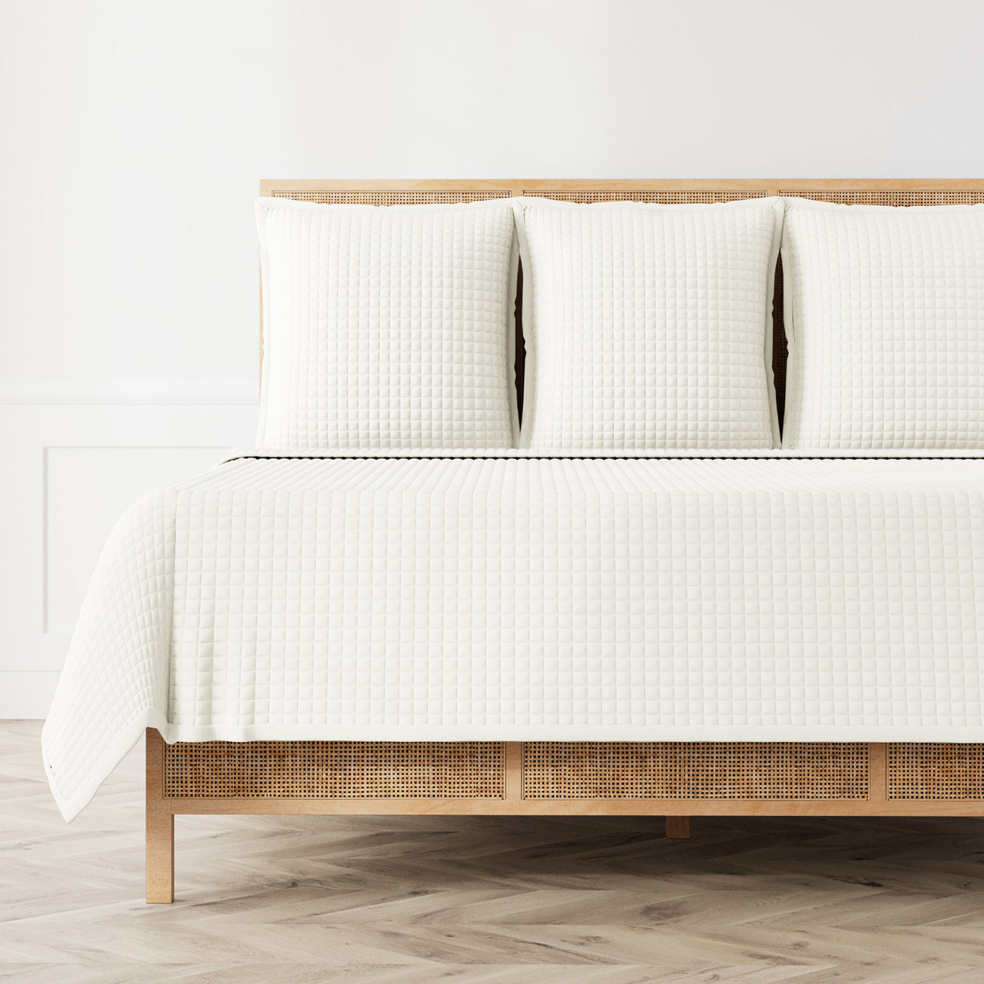 Ivory quilted coverlet and shams on a rattan bed, showing full bed styling.