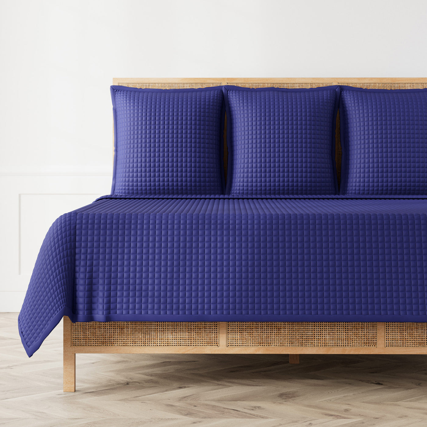 Royal blue Ann Gish quilted coverlet with grid texture on a rattan bed, three matching shams.