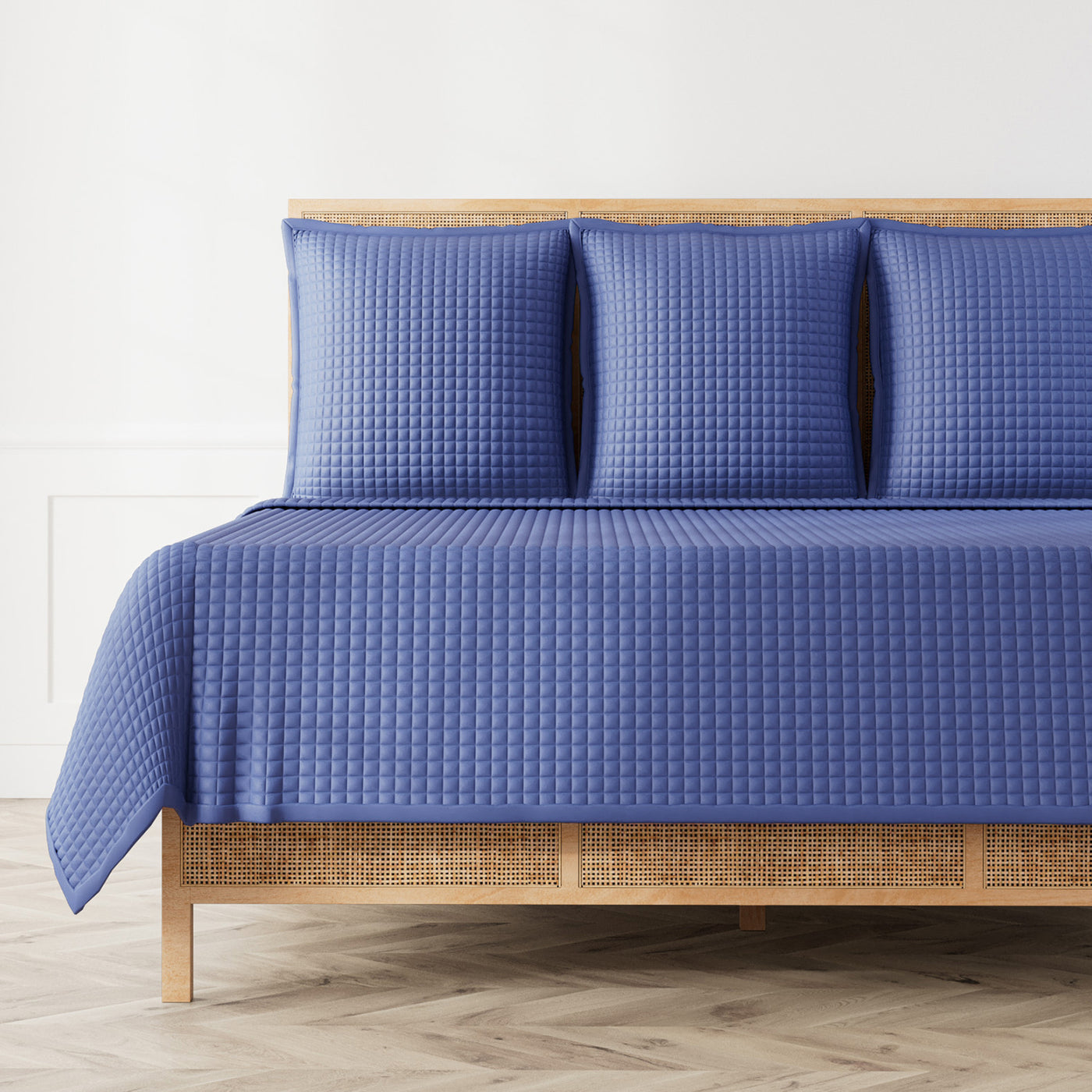 Ann Gish Ready-to-Bed 2.0 coverlet in blue, waffle-quilted texture styled on a rattan bed.