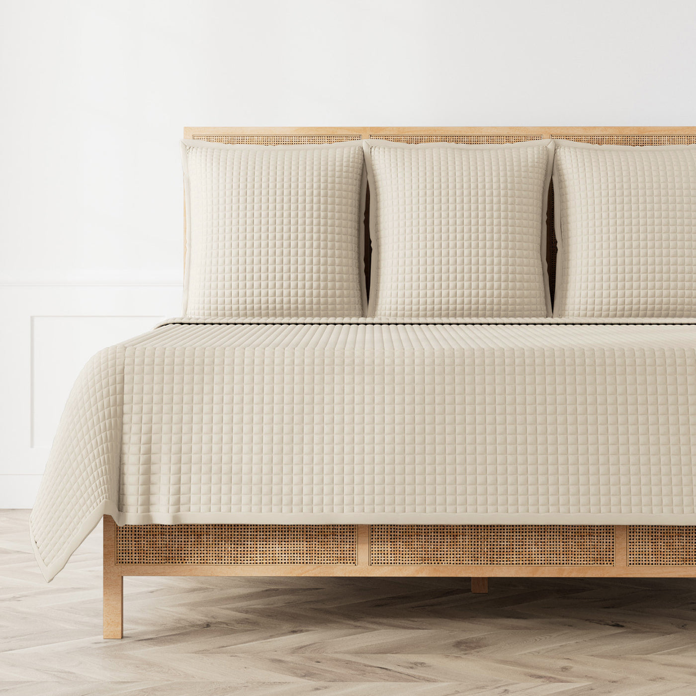 Ivory quilted coverlet with grid texture draped over a rattan bed with matching shams.