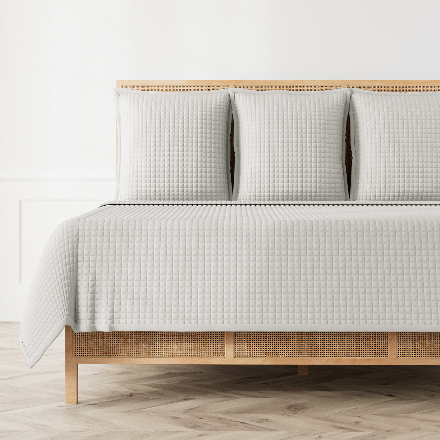Silver-grey quilted coverlet and matching shams styled on a rattan bed frame.