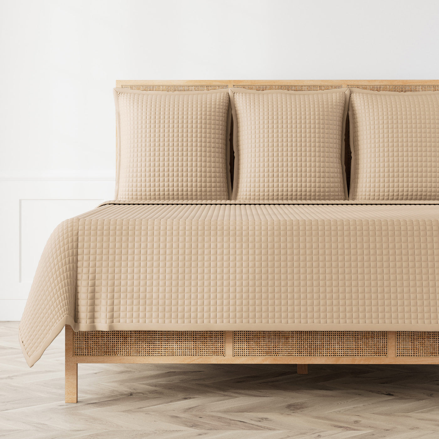 Waffle-quilted linen coverlet in sand draped over a rattan bed with matching shams.