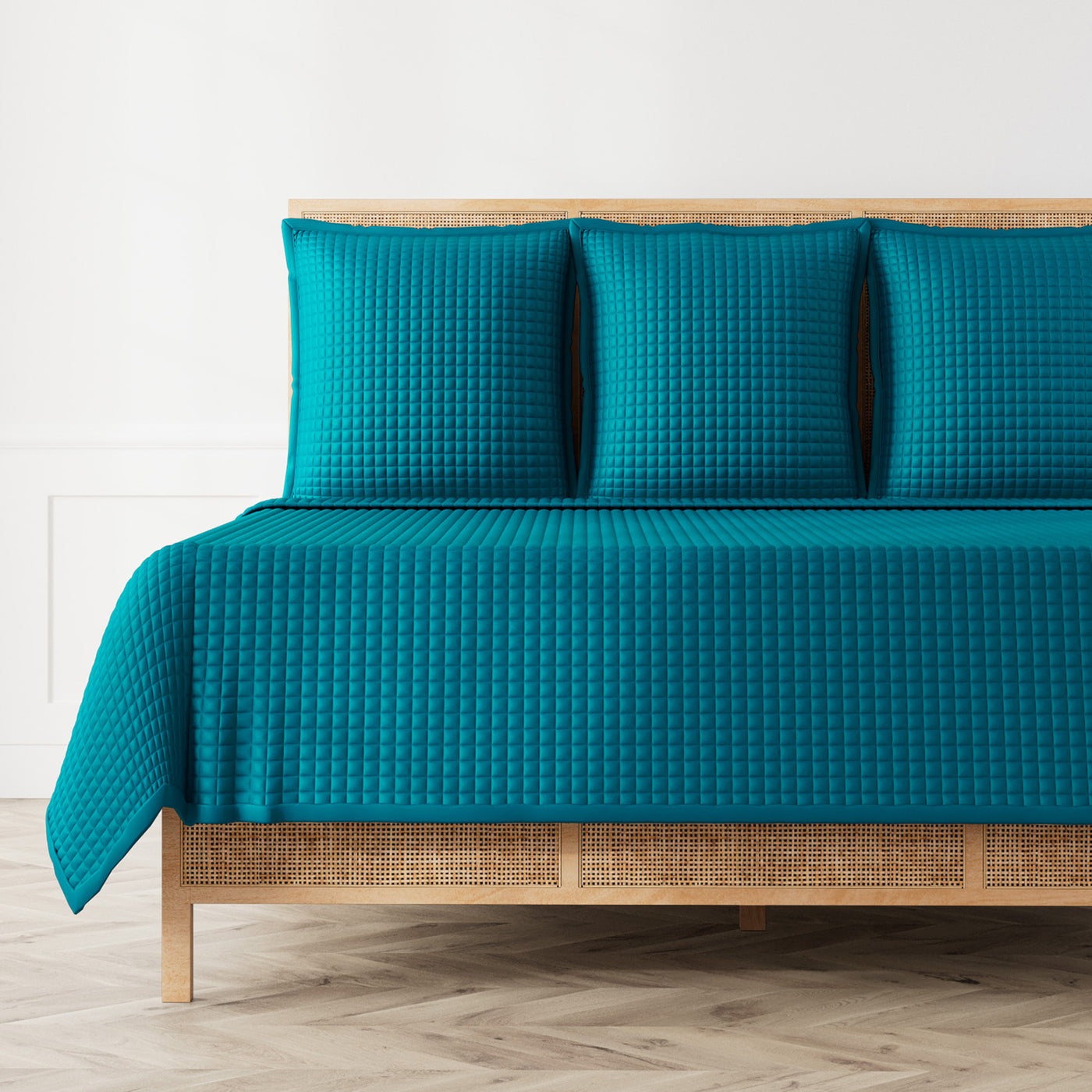 Teal quilted coverlet and matching shams on a rattan bed, herringbone floor.