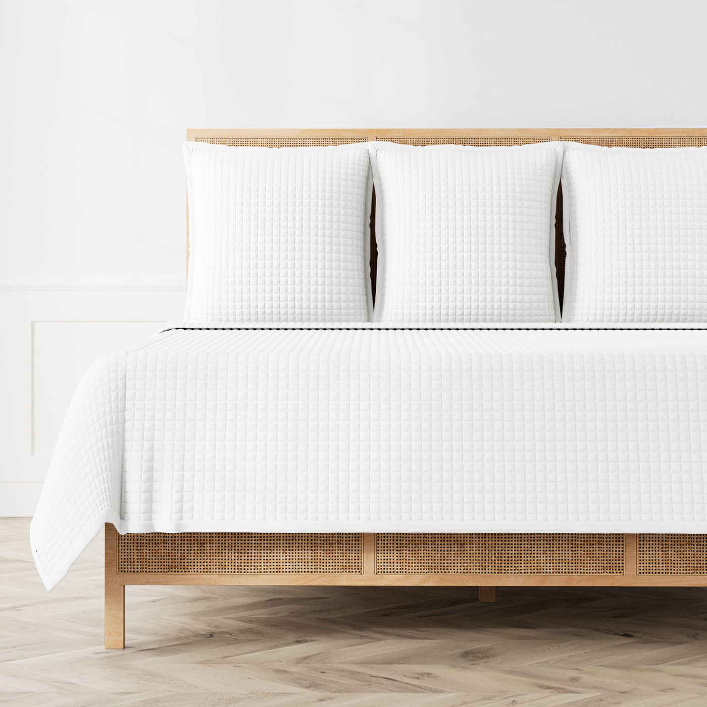 White quilted coverlet on rattan bed, textured waffle pattern, styled with matching shams.