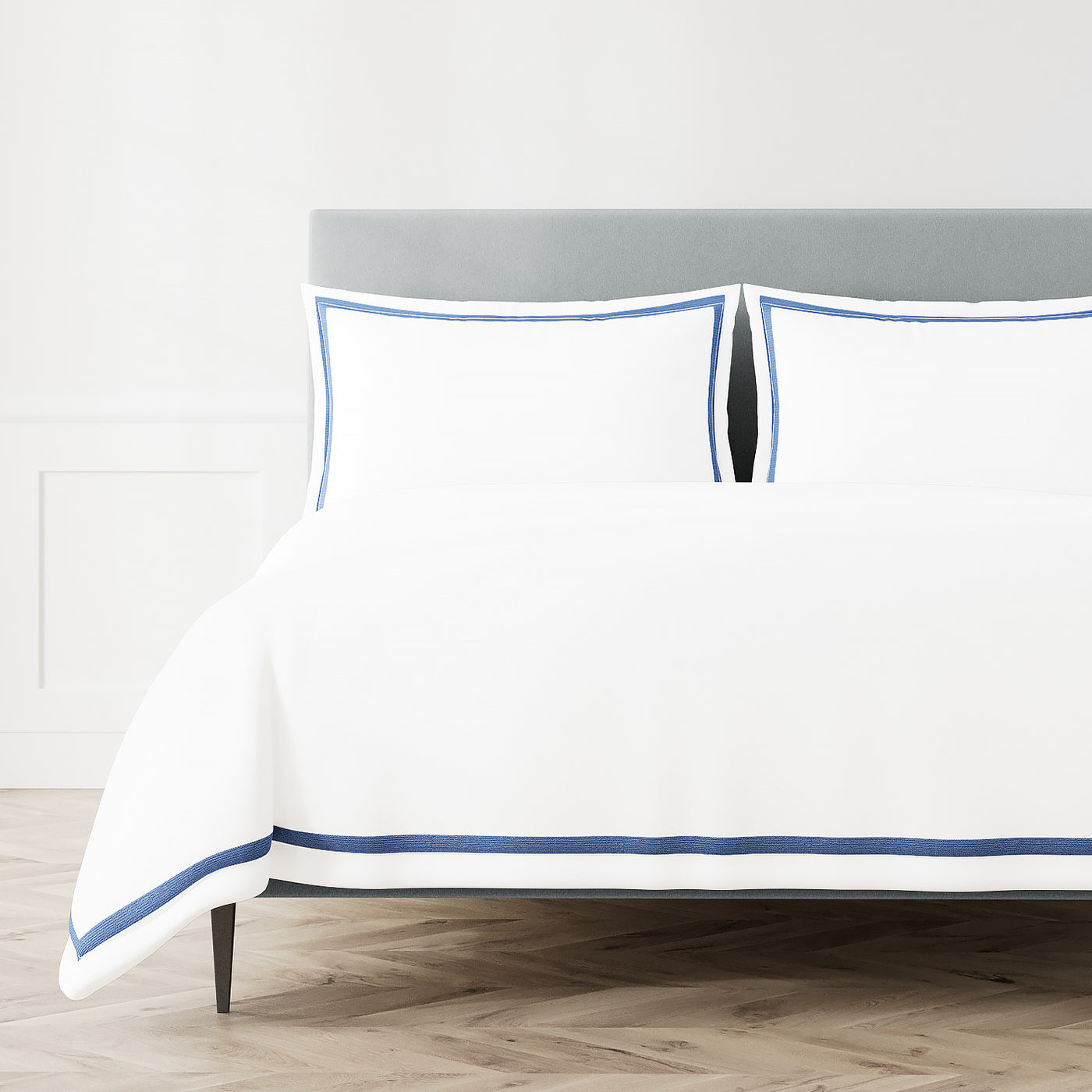 White Ann Gish duvet cover with blue trim border, styled on bed with matching shams.