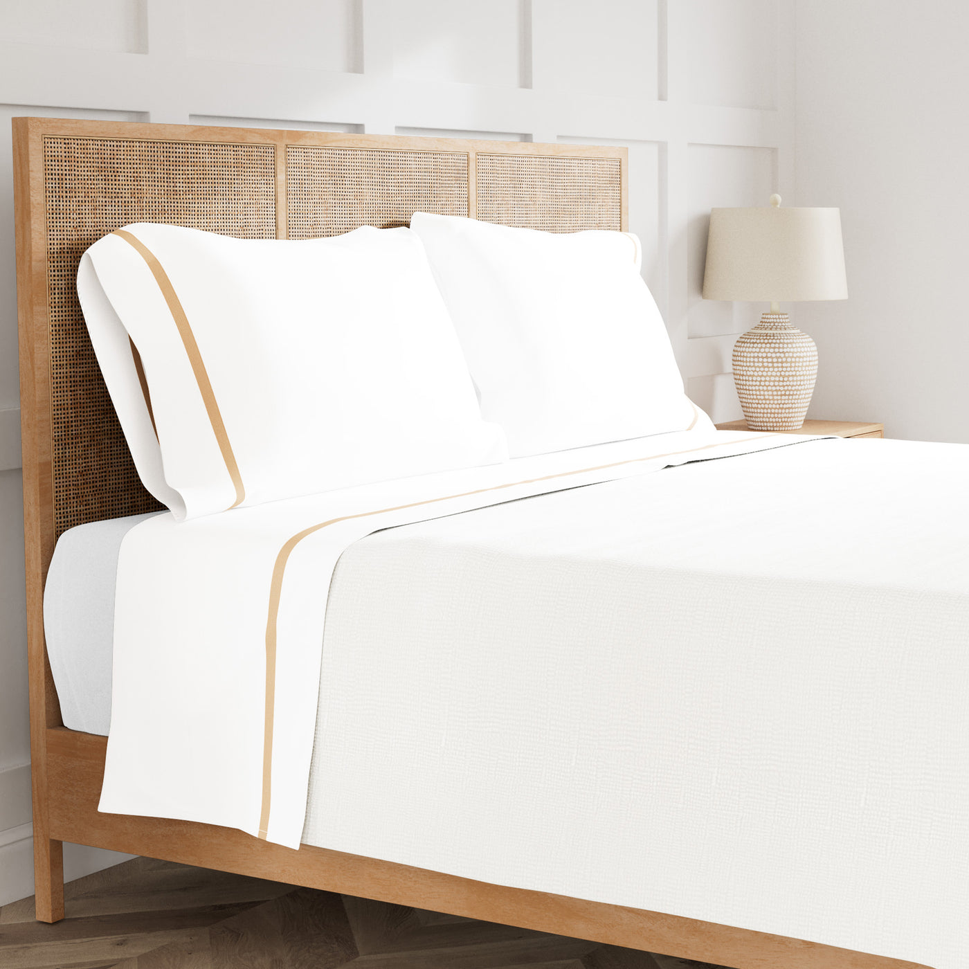 White cotton sheet set with honey trim detail, styled on rattan bed with lamp on nightstand.
