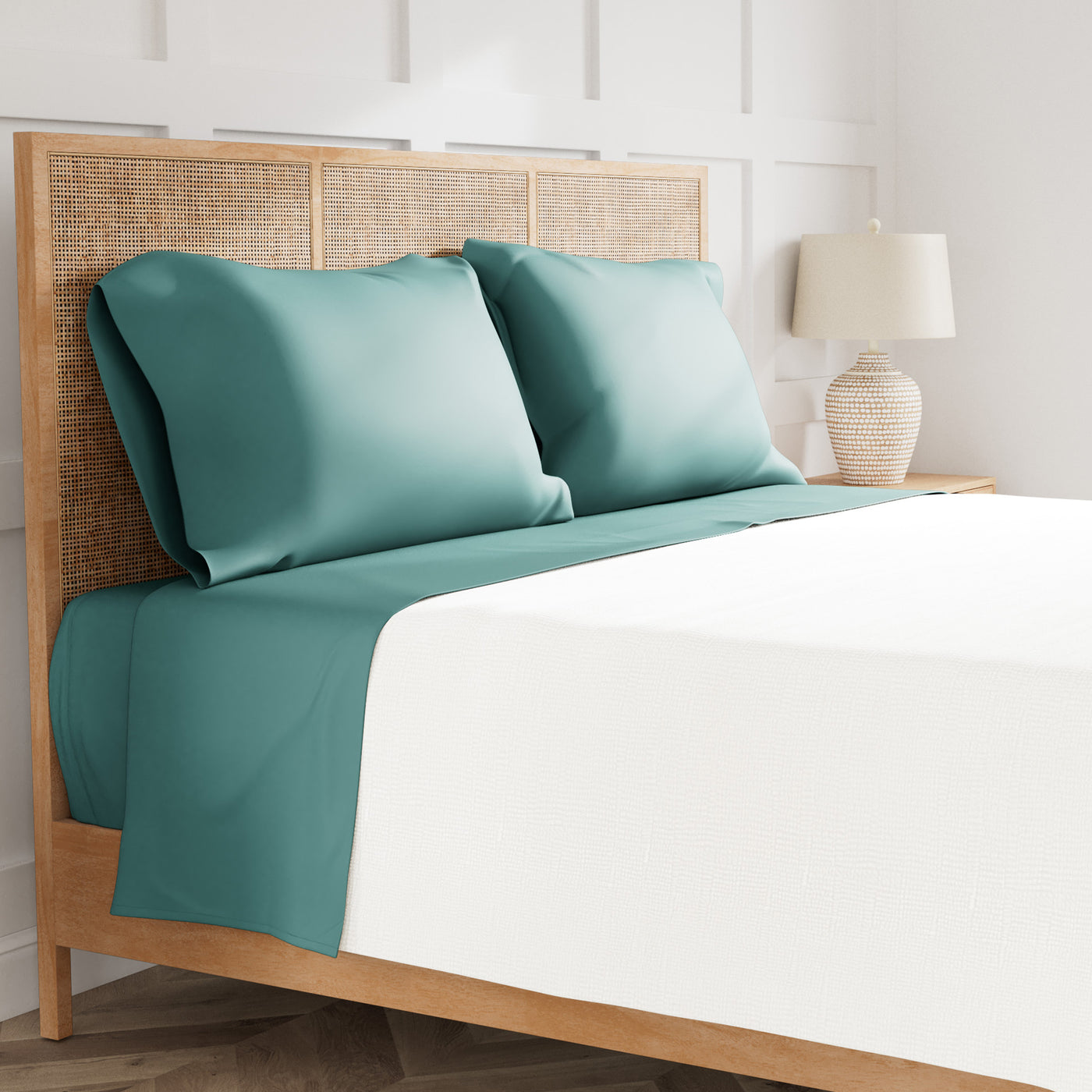 Teal satin-finish pillowcases and flat sheet on a rattan bed with white fitted sheet.