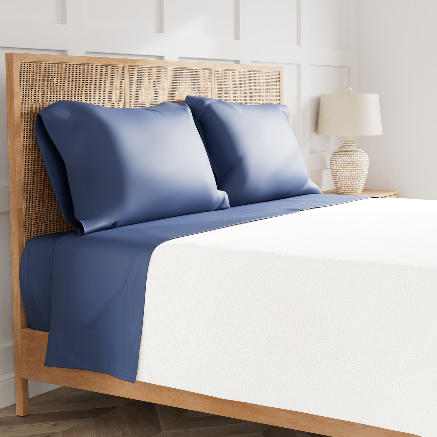 Navy blue satin pillowcases and flat sheet on a rattan bed, white duvet cover.
