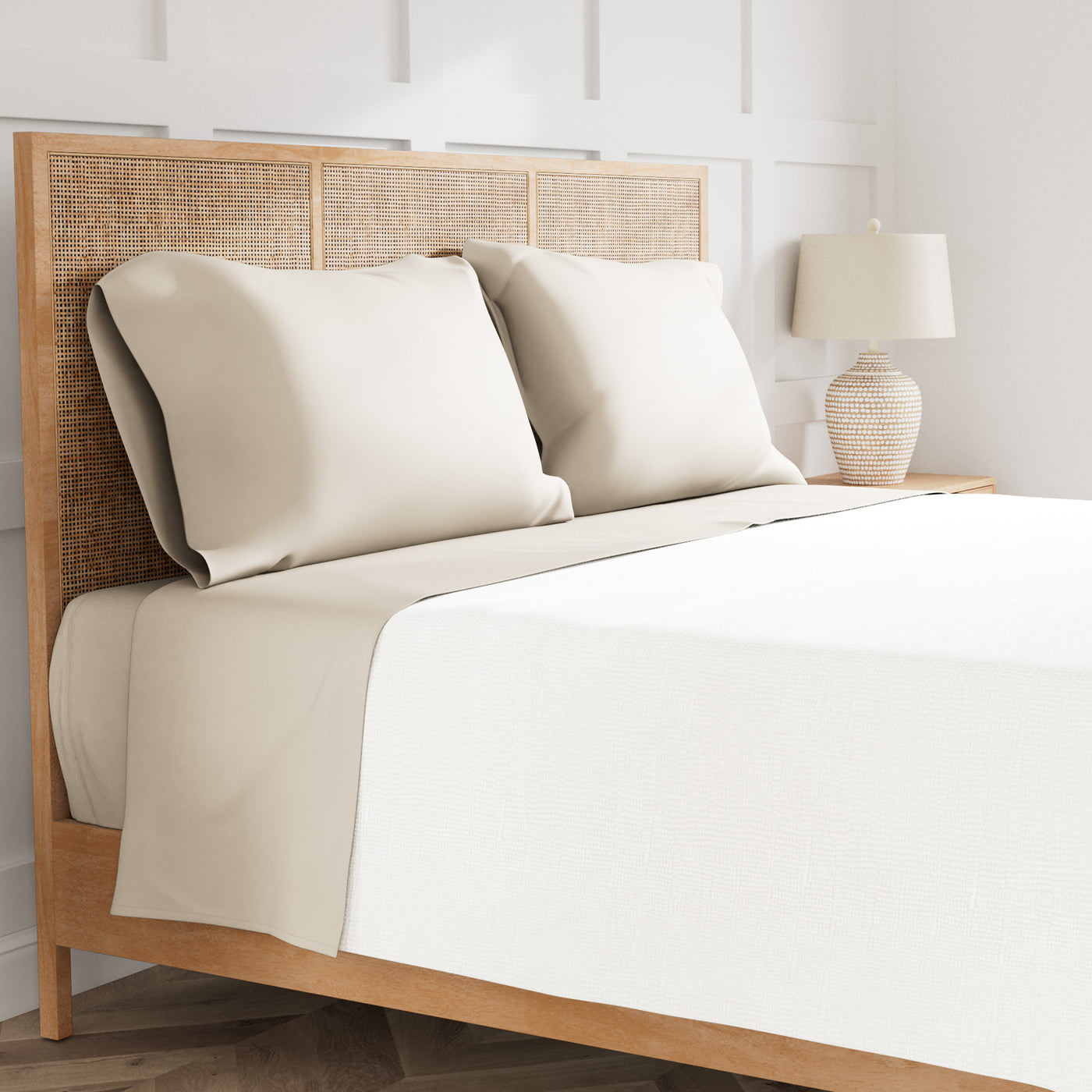 Ivory and sand sheet set on rattan bed with two pillows and bedside lamp.