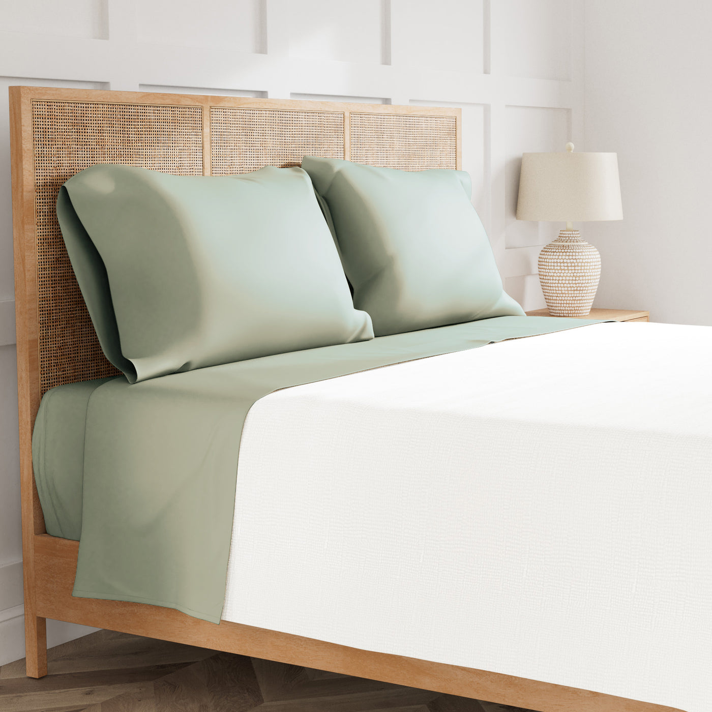 Sage green pillowcases and flat sheet on a rattan headboard bed, styled with ivory bedding.