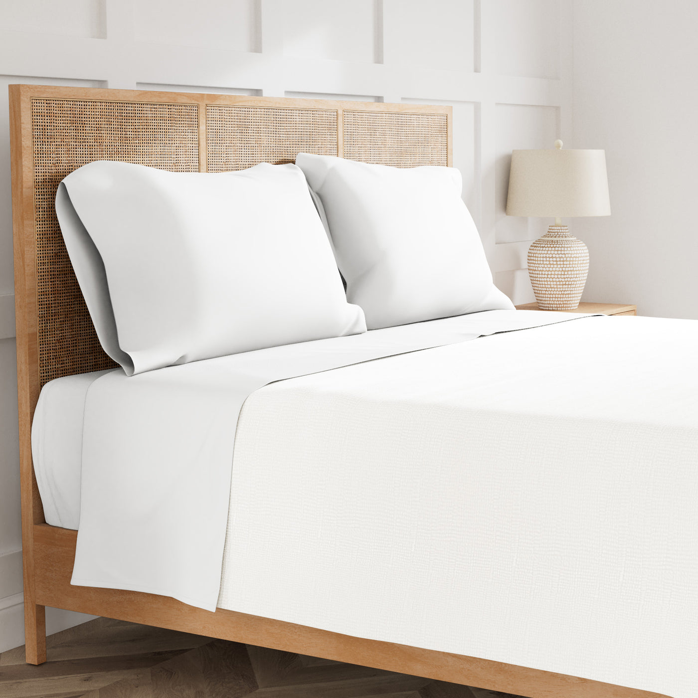 White Ann Gish Ready-to-Bed 2.0 sheet set styled on a rattan bed with two pillows.