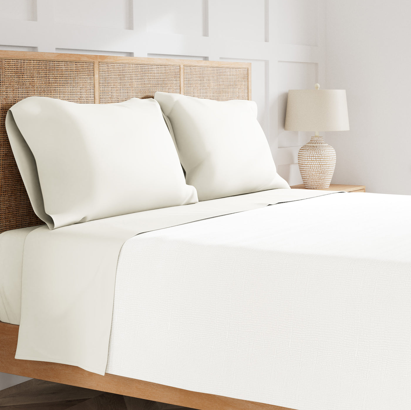 Ivory sheet set styled on bed with rattan headboard, flat sheet folded over duvet.