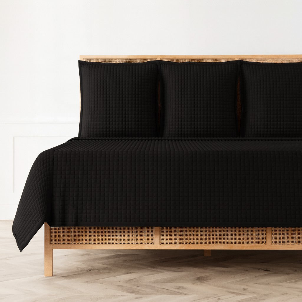 Black quilted coverlet and matching shams on a rattan bed, herringbone floor.