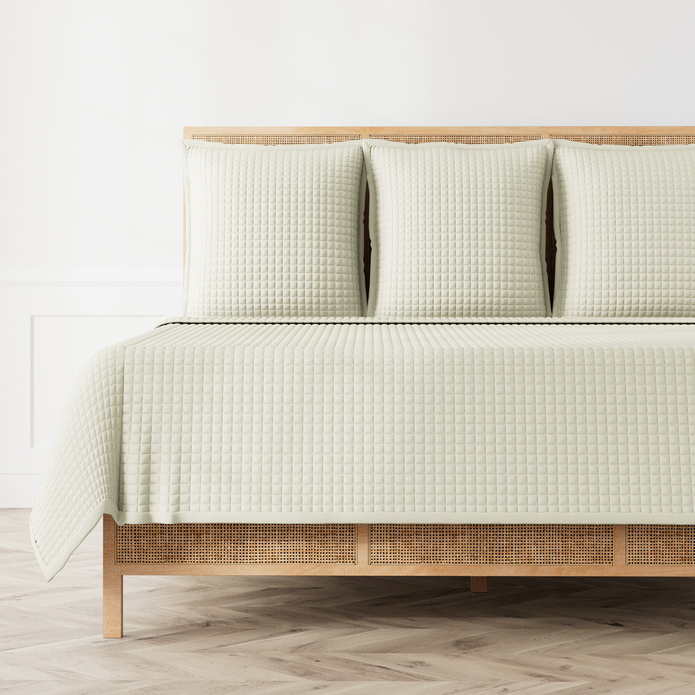Sage quilted coverlet and shams on a rattan bed frame, full bed view.