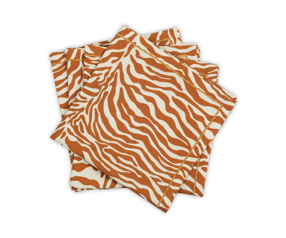 Four cloth napkins from the Regine | Napkin Set by Matouk, featuring an orange and white zebra motif, are stacked on a white background as part of their Schumacher decorative printed linen collection.