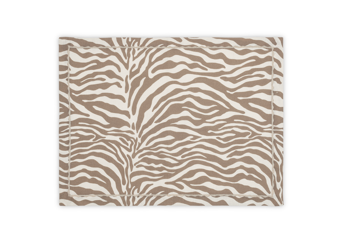 The Regine Placemat Set by Matouk features a beige and white stylized zebra motif with a simple stitched border. Part of the Schumacher table collection, it's shown on a white background.