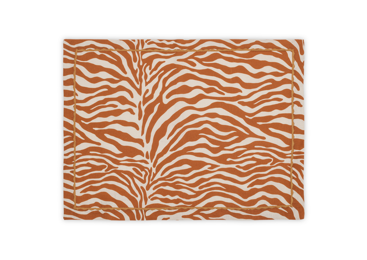 The Regine Placemat Set by Matouk features a stylized orange and white zebra motif on printed linen, inspired by the Schumacher table collection.