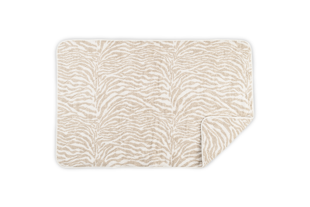 The Regine Quilted Tub Mat by Matouk, shown on a white background with one corner folded, features a beige and white zebra pattern and is crafted from a linen-cotton blend.