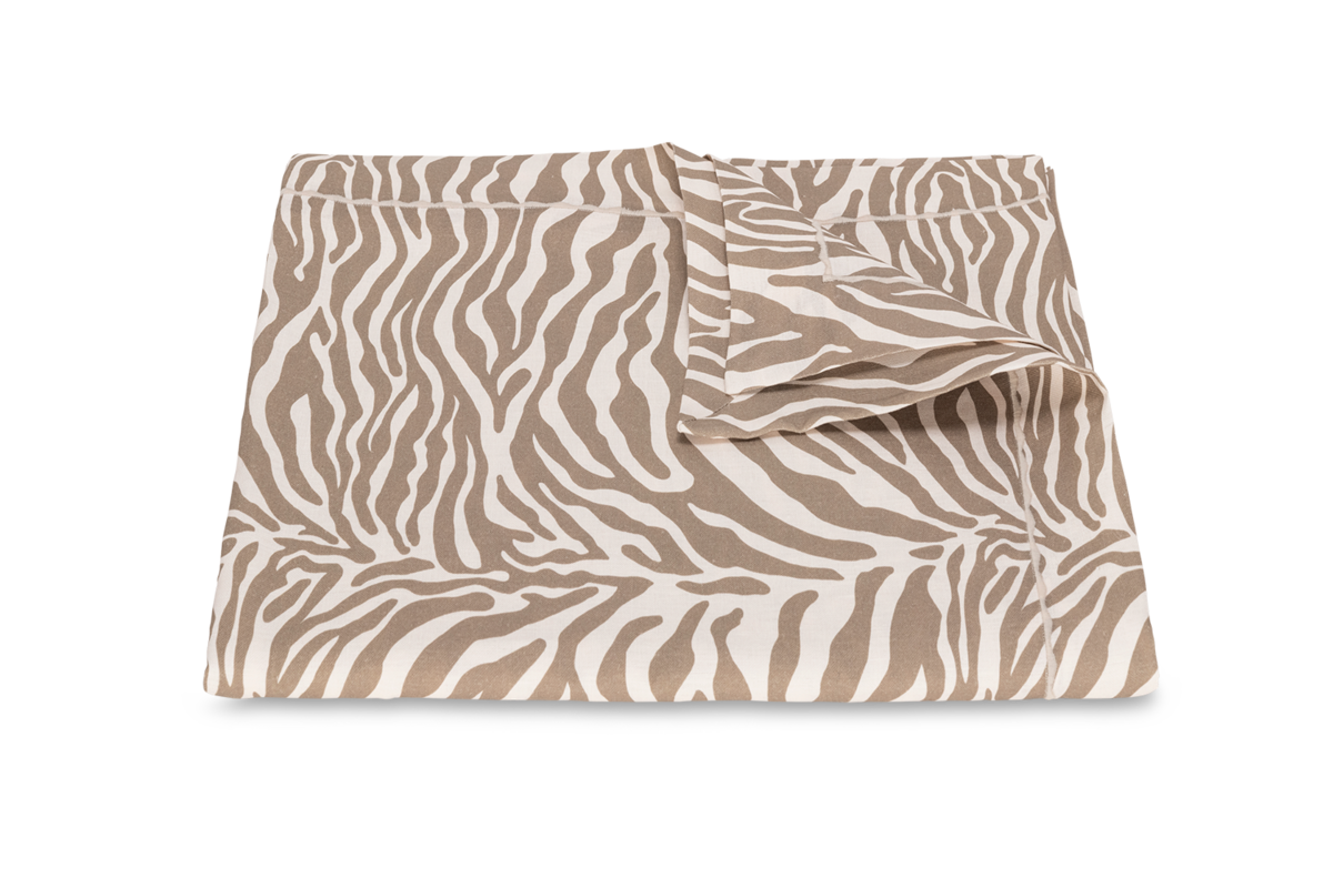 The Matouk Regine tablecloth is shown folded on a plain background, highlighting its decorative printed linen design with a beige and white zebra motif.