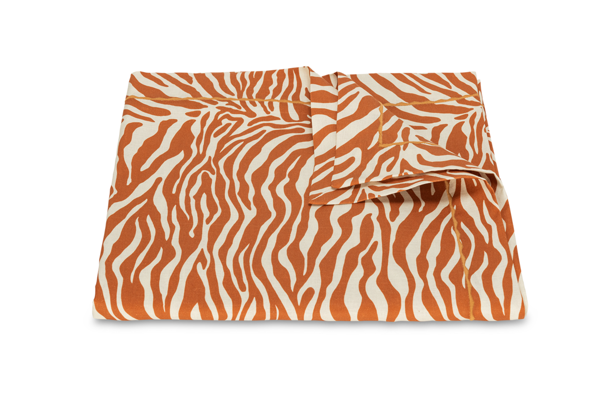 The Regine | Tablecloth by Matouk showcases folded fabric with an orange and white zebra motif on a plain white background—ideal as decorative printed linen for stylish table settings.