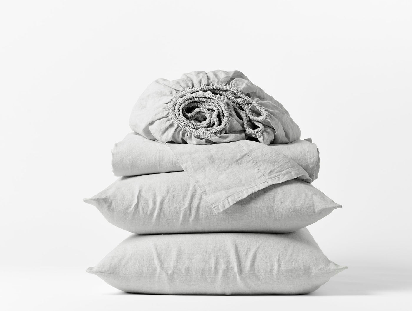 Rolled fitted sheet atop folded flat sheet and two stacked pillowcases in silver grey linen.