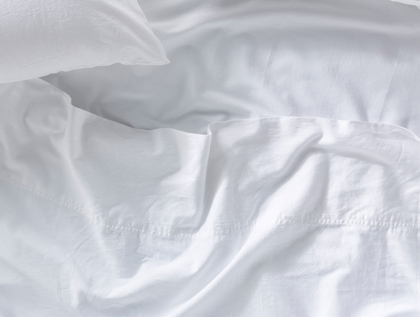 Softly draped white sateen sheets with a pillowcase, showing luminous fabric sheen.