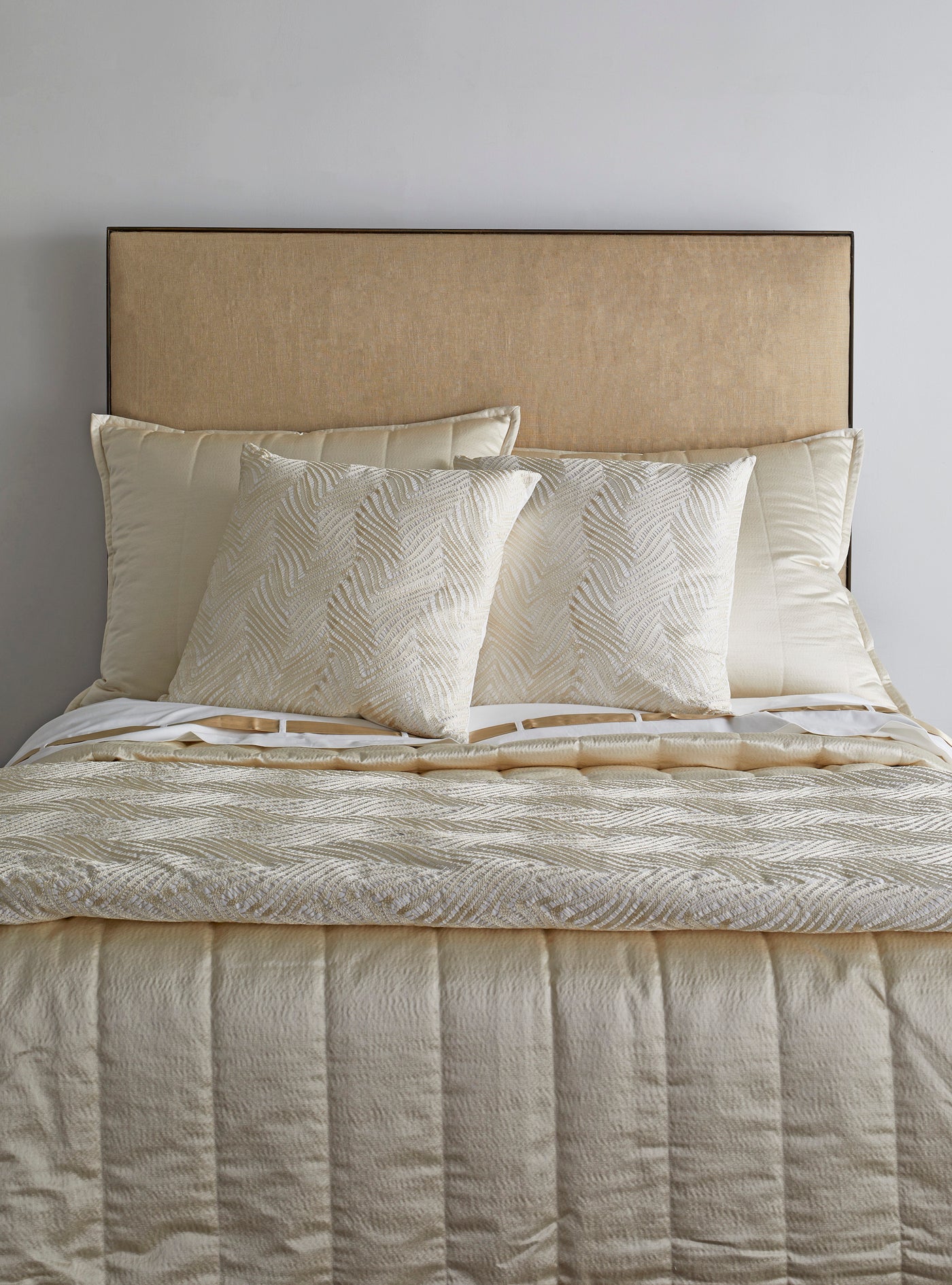 Close-up of Ann Gish Retortoli pillow in ivory with textured leaf pattern on styled bed.