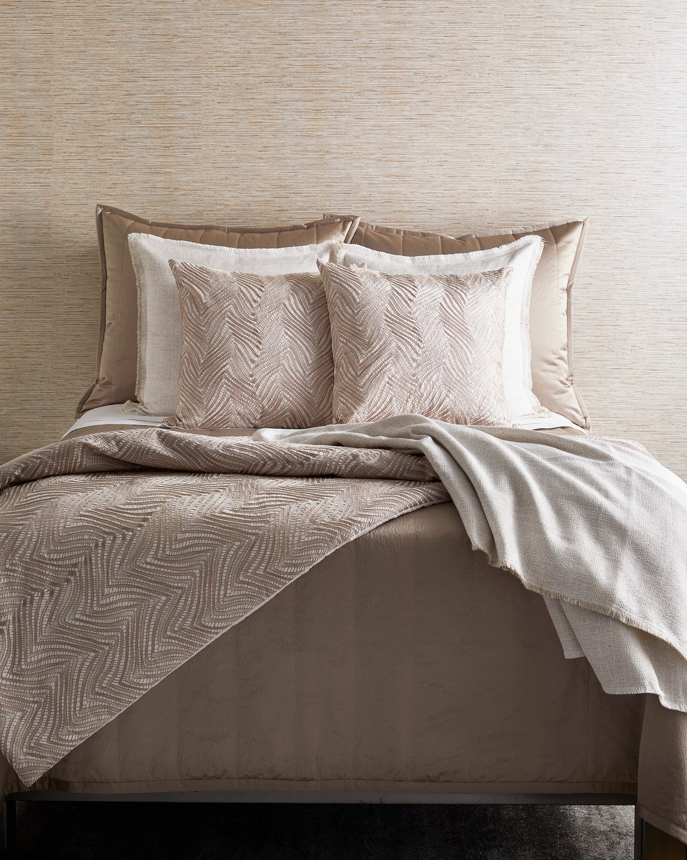 Ivory throw draped over champagne herringbone quilt on styled bed with textured Euro shams.