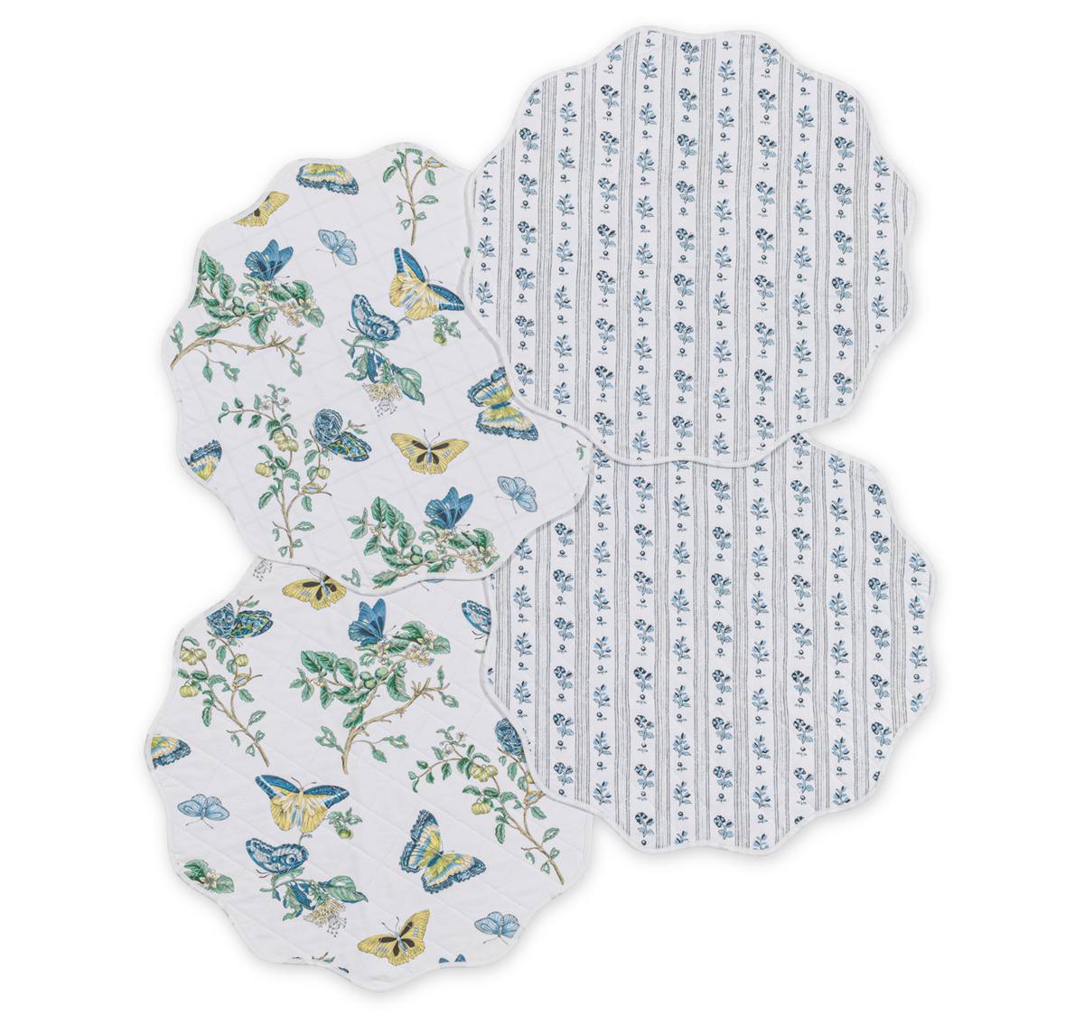 The Matouk Quilted Reversible Placemat Set features four scalloped placemats—two in a blue floral and butterfly pattern, and two with blue vertical floral stripes—overlapping on a white background for stylish table decor.