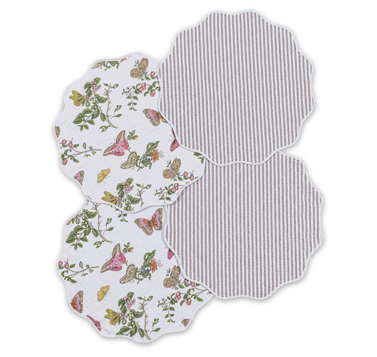 The Matouk Quilted Reversible Placemat Set features four scalloped-edge placemats—two with a floral and butterfly print, two with gray and white stripes—arranged in an overlapping display for stylish dining decor.