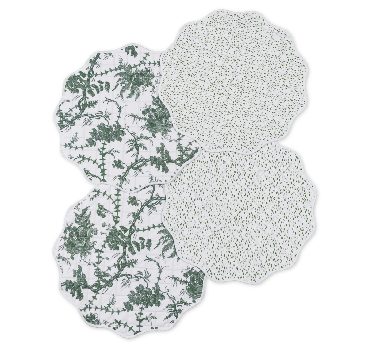 The Matouk Quilted Reversible Placemat Set includes four scalloped-edge placemats—two with a green floral pattern and a reversible side featuring small green dots—ideal for adding style to your dining table.