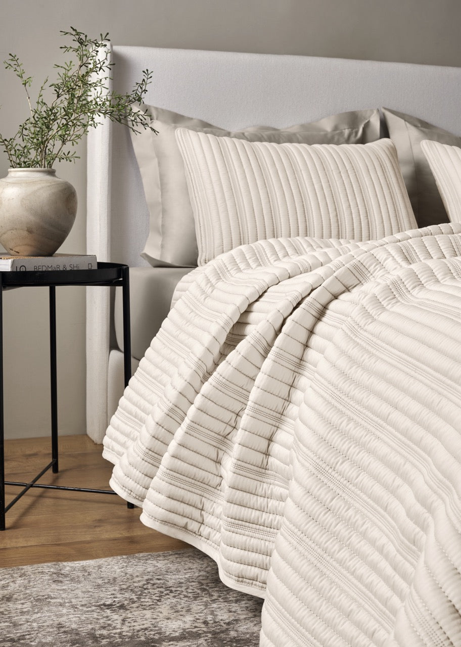 Close-up of Ann Gish Rib coverlet in ivory with textured ribbed channels on a styled bed.