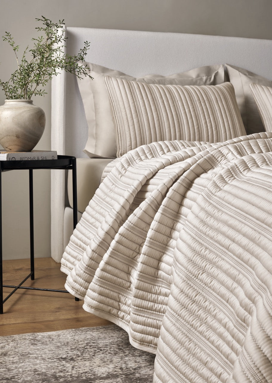 Ivory ribbed coverlet draped over bed with matching pillow, neutral bedroom styling.