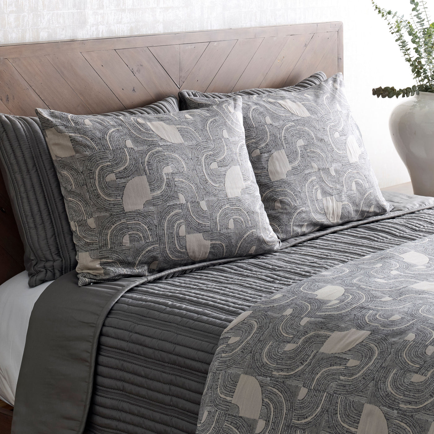 Charcoal ribbed coverlet layered with paisley-print shams on a styled bed.