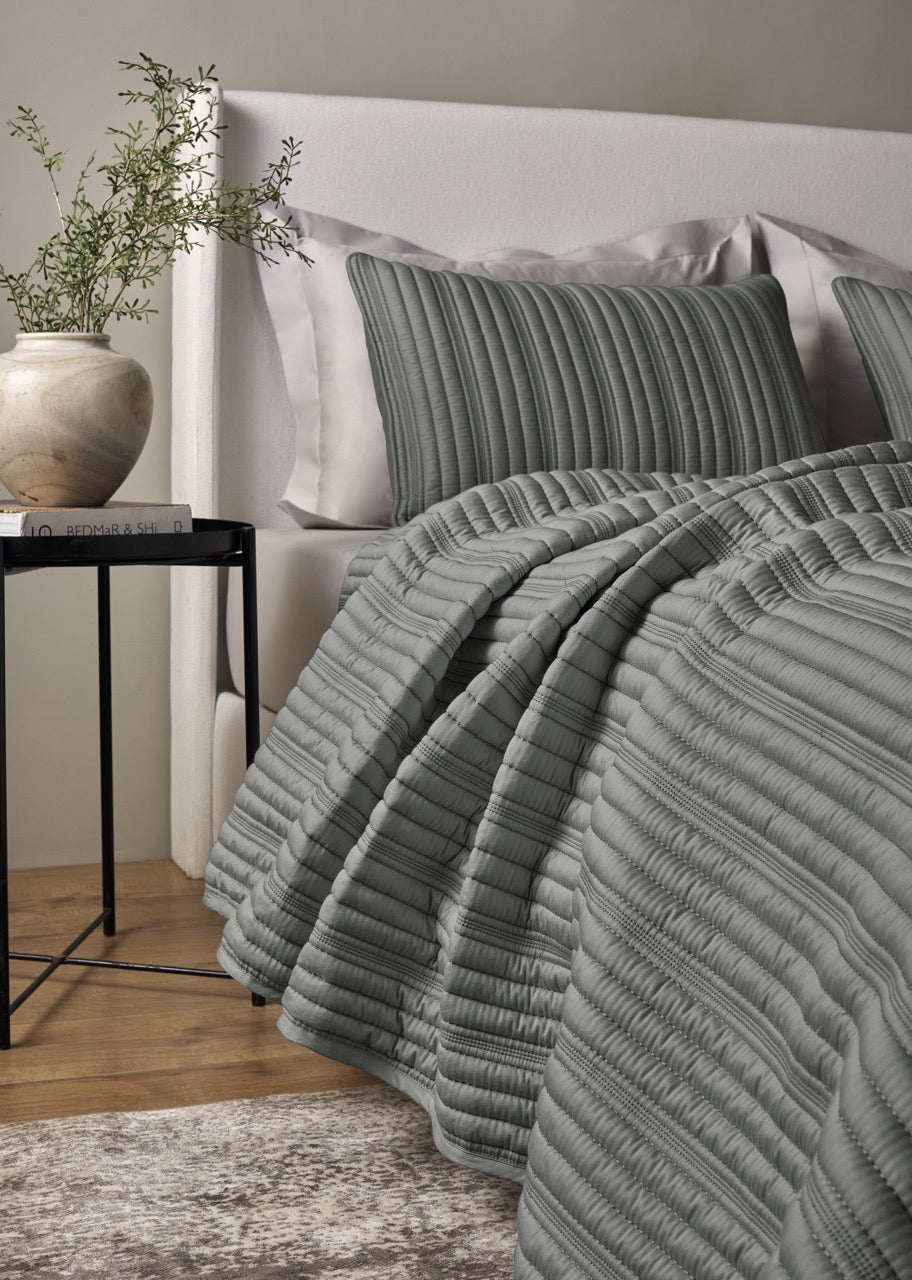 Sage green ribbed coverlet draped over bed, showing pleated texture detail with matching sham.
