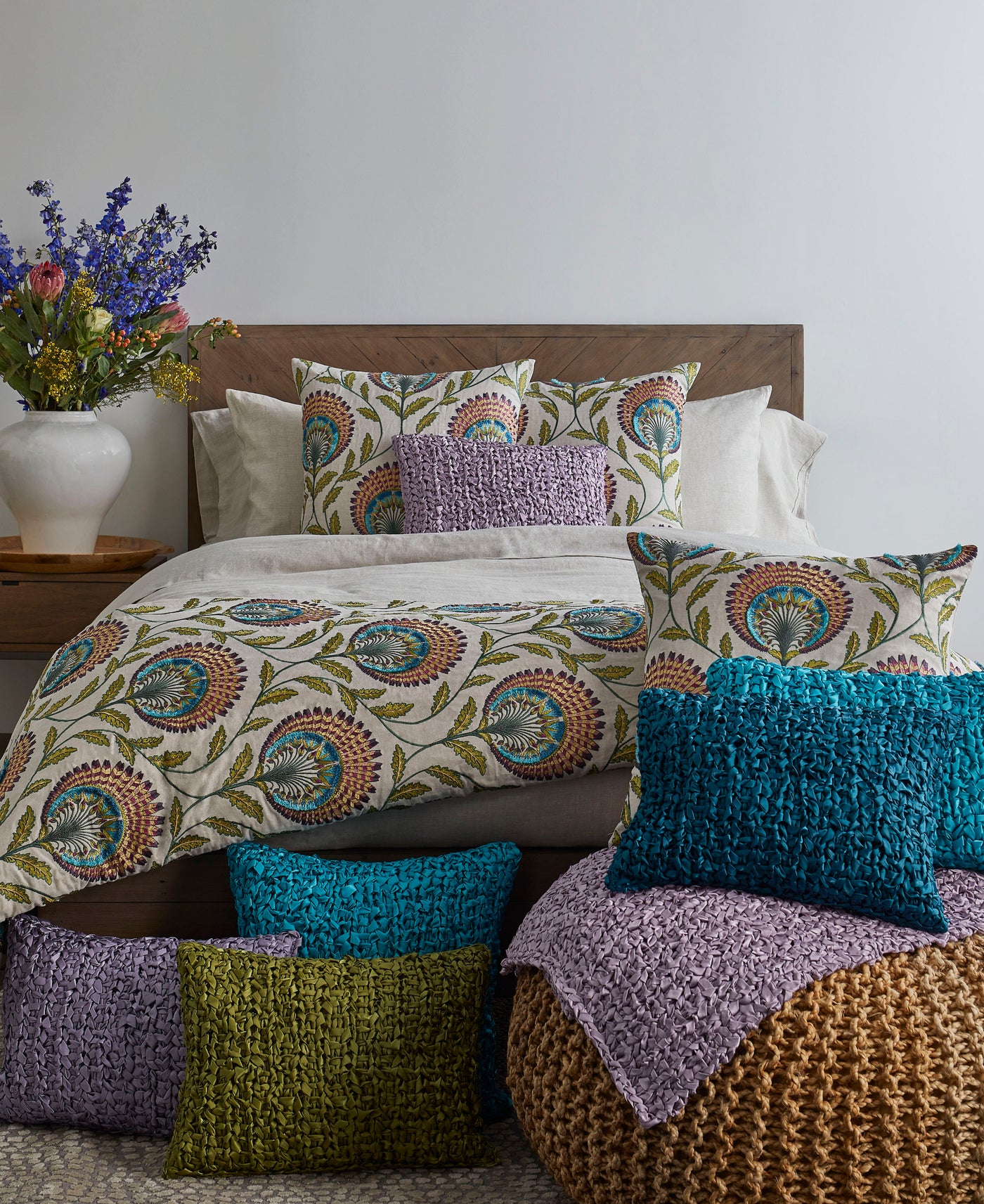 Teal, olive, lavender, and mauve Ribbon Knit pillows styled on and around a patterned bed.