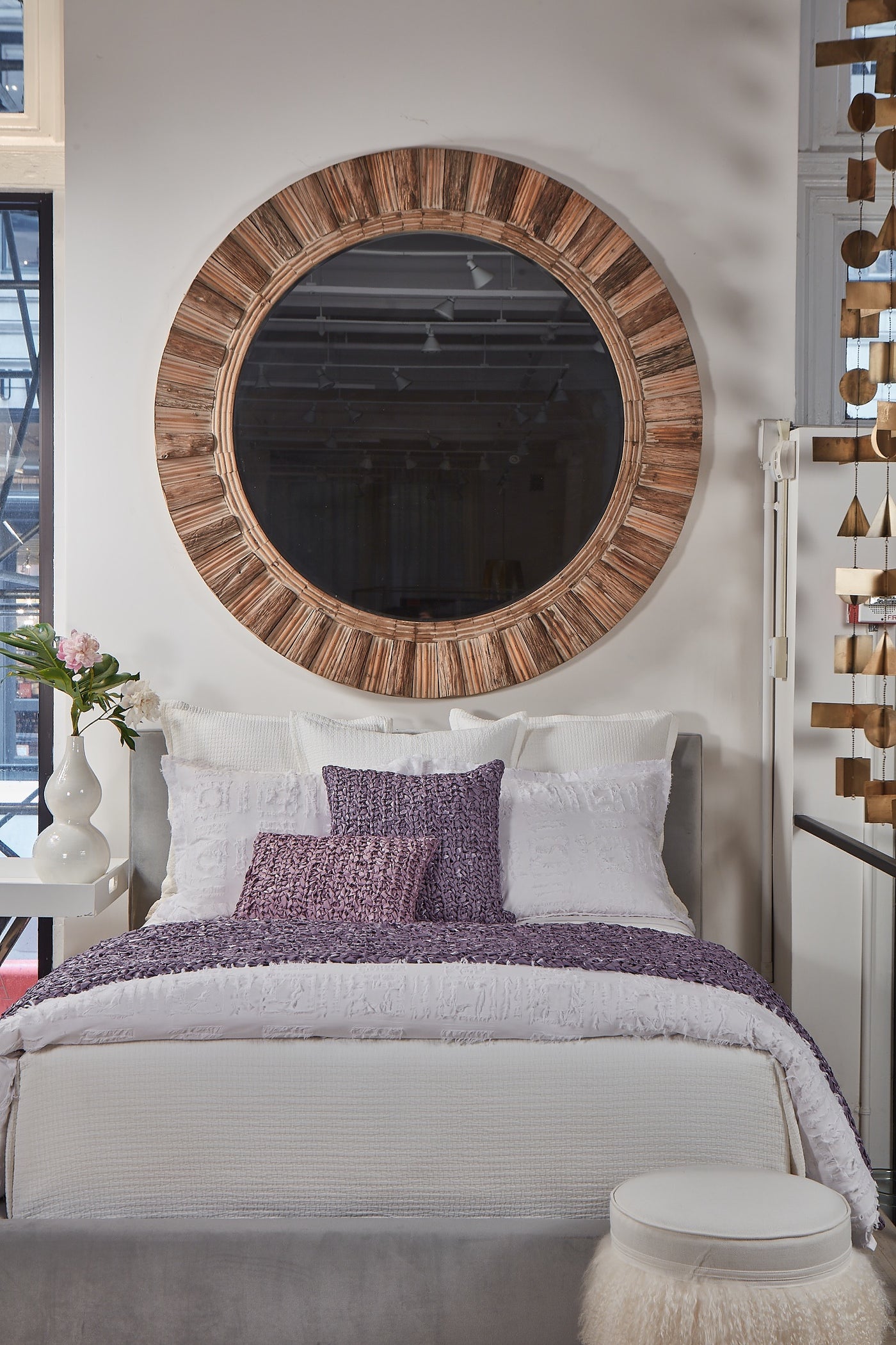 Amethyst knit pillow styled on a made bed with white bedding and a large round mirror above.