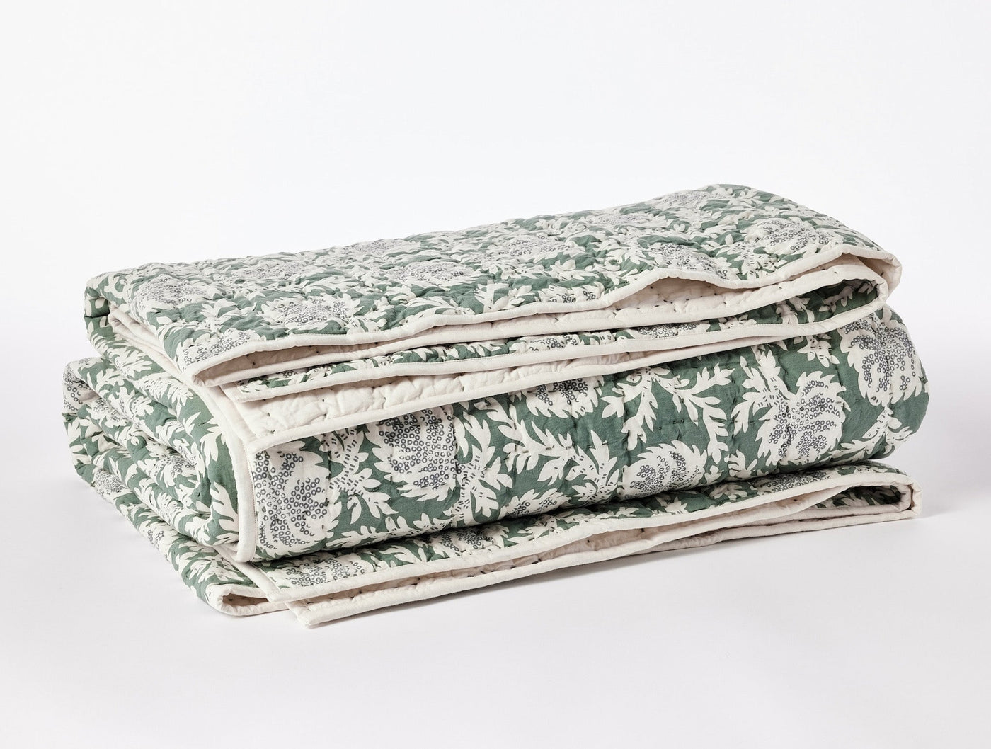 Folded Coyuchi quilt showing green and ivory floral block-print pattern and handstitched edges.