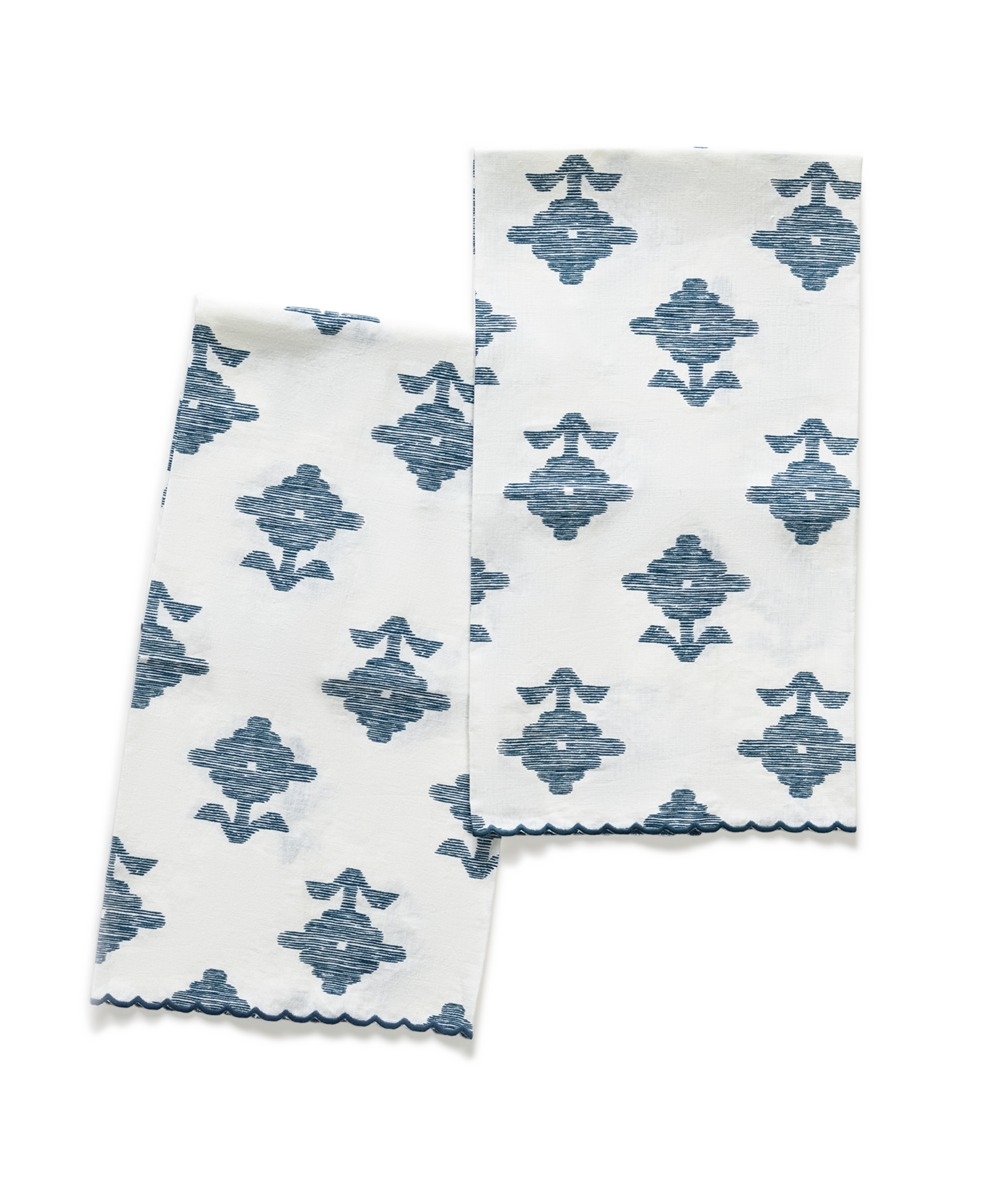 Two Matouk Rubia Guest Towels, white with blue Schumacher geometric embroidery and scalloped edges, are laid out on a white surface.