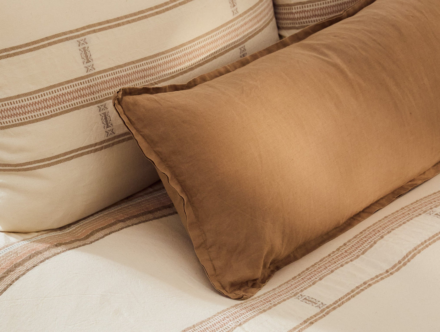 Caramel linen decorative pillow styled against ivory striped bedding.