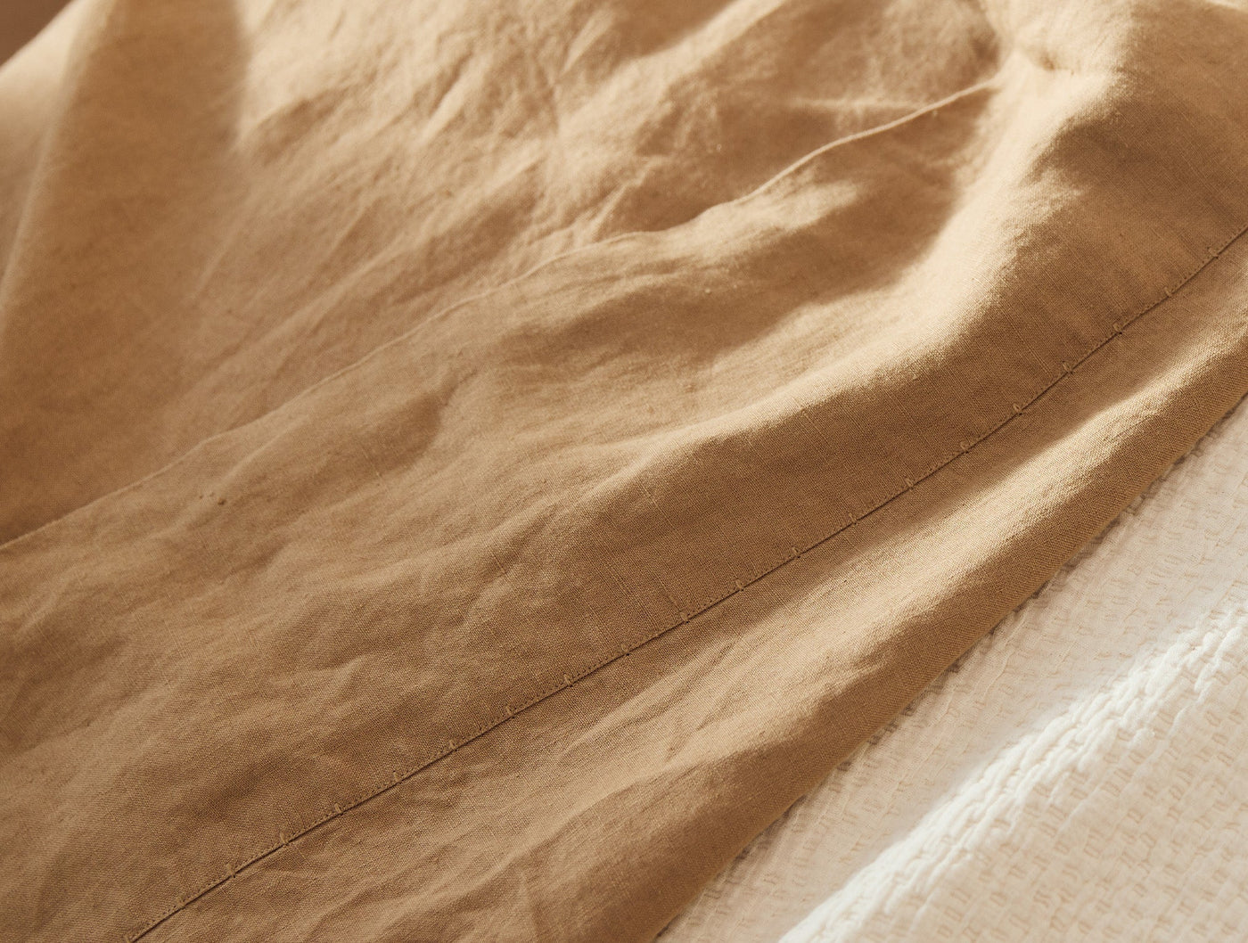 Close-up of caramel linen pillowcase hem, showing relaxed natural drape and texture.