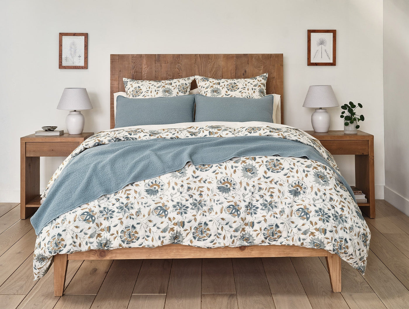 Dusty blue matelasse blanket draped over floral bedding in a styled bedroom setting.
