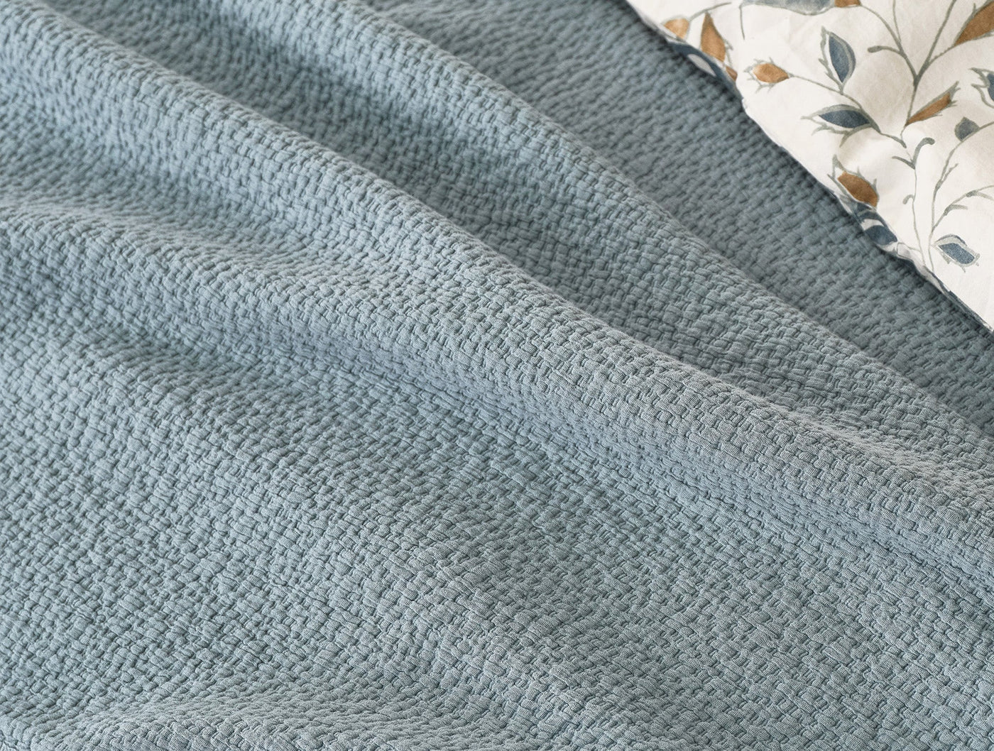 Close-up of Coyuchi Cascade Matelasse blanket in slate blue with woven texture detail.