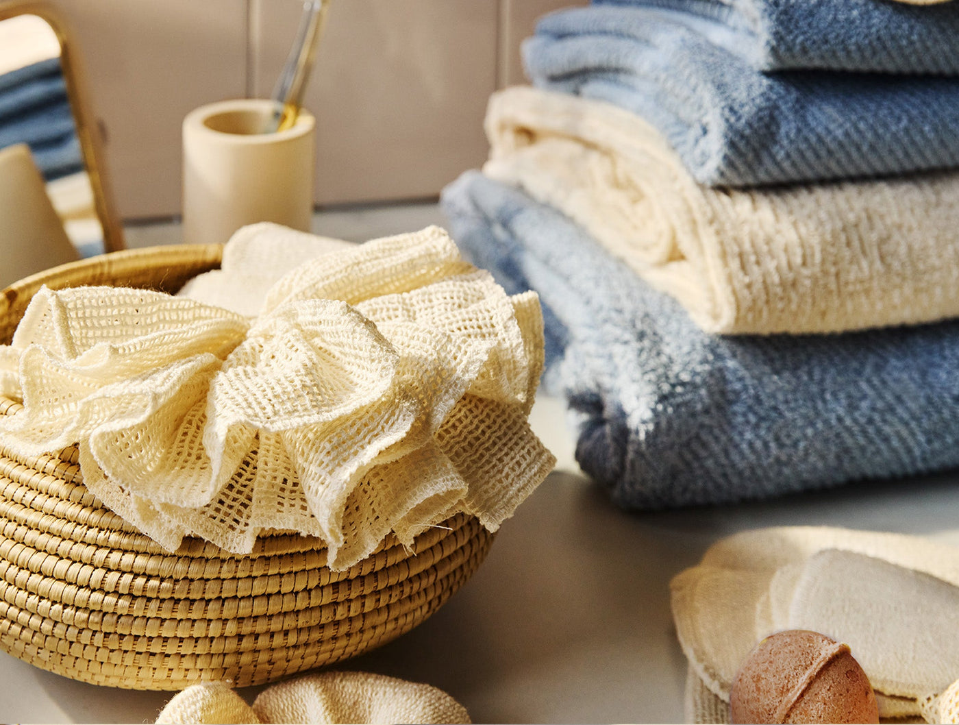 Ivory crochet loofah draped in a woven basket, styled with folded blue and ivory towels.