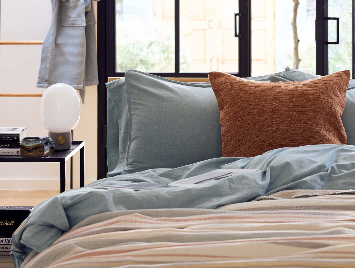 Sage crinkled percale pillowcases styled on a bed with a rust textured throw pillow.