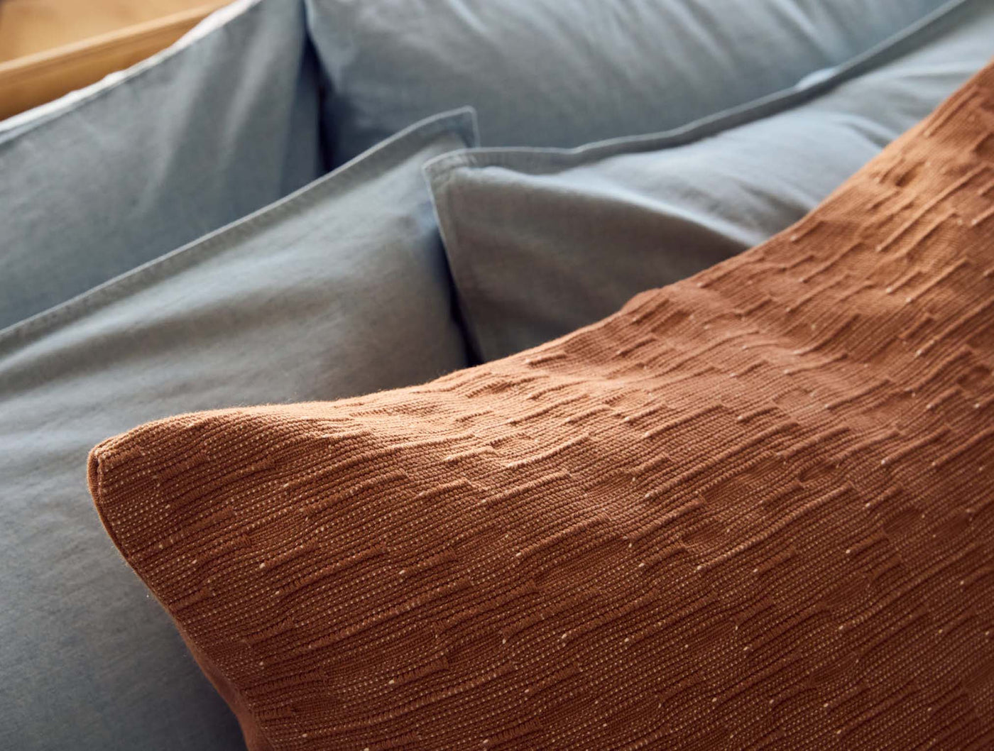Close-up of Coyuchi Toro Canyon pillow's terracotta textured weave against slate linen pillows.