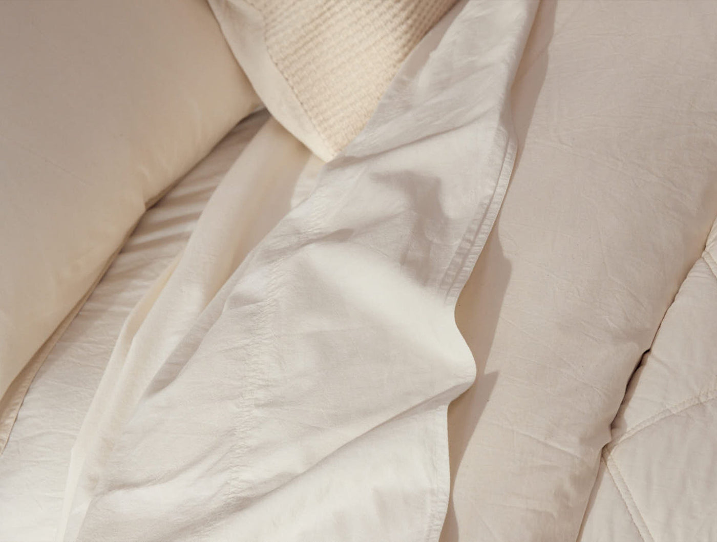 Ivory crinkled percale sheets draped loosely, showing relaxed texture and natural folds.