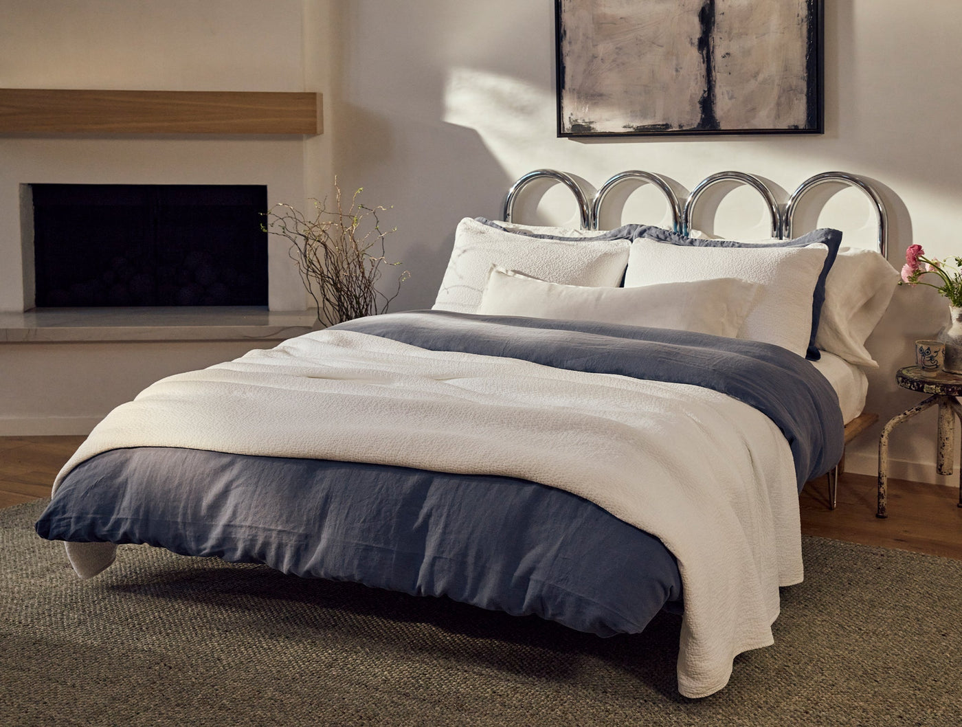 Ivory matelasse blanket layered over navy bedding on a styled bed with fireplace backdrop.