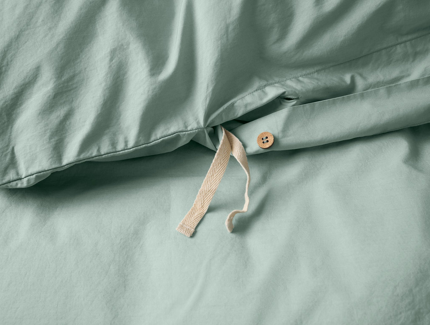 Close-up of sage percale duvet cover with natural cotton tie closure and wooden button detail.