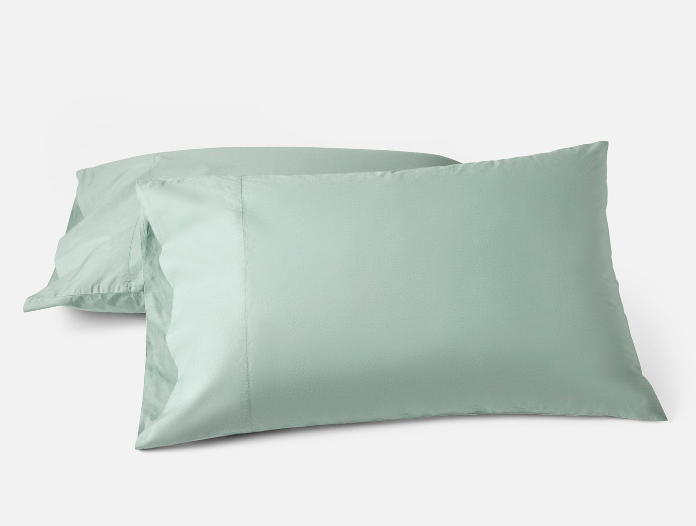 Two sage green Coyuchi Refined Percale pillowcases stacked against a white background.